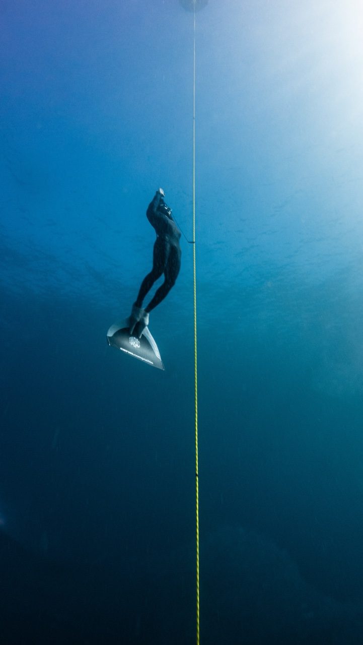Freediver in professional equipment ascending beside a depth line